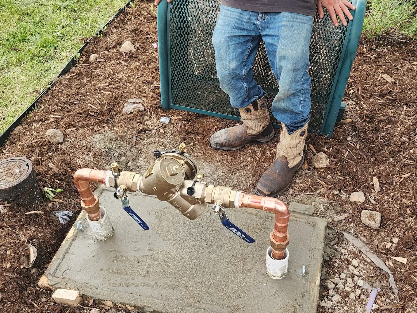 Plumber examining a water meter. Copper pipes and valves are visible in dirt.