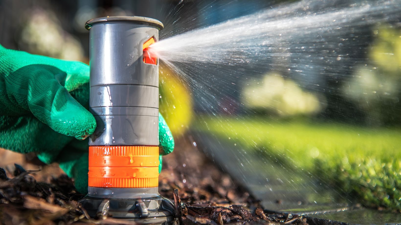 Hand holding a sprinkler, spraying water in a garden, watering the lawn.